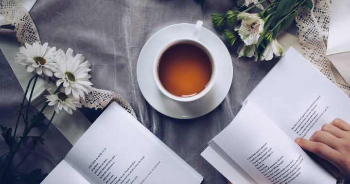 white ceramic teacup with saucer near two books above gray floral textile